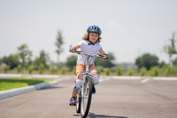 Poster - Kid riding bike on a summer park. Child in safety helmet riding bike. Boy riding bike wearing a helmet outside. Child in safety helmet riding bike. Little kid boy learns to ride a bicycle.