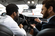 © sofiko14 - Dealer explains the car dashboard features to potential customer creating engaging and informative interaction. Caucasian car dealer sit inside vehicle with African American buyer.