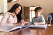 © SensSai/peopleimages.com - Learning, mother and boy with tablet, education and creative assignment for child development with parent. Home, student and book to practice handwriting, ebook and mom helping with art project