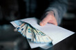 © Igor - Man hand giving an envelope full of euros banknotes.