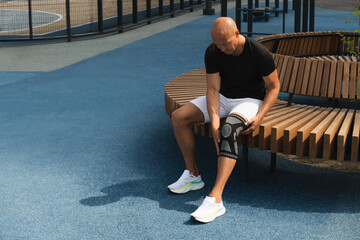 Man putting knee brace to support painful leg. Athlete bodybuilder leg wearing knee support brace or elastic kneecap bandage. Sleeve for compression. Health problems and pain.