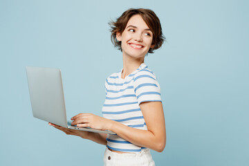 Wall Mural - Side view smart young IT woman wear striped t-shirt casual clothes hold use work on laptop pc computer look aside isolated on plain pastel light blue cyan background studio portrait Lifestyle concept