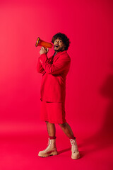 Wall Mural - A young Indian man in a vibrant red suit holding a red megaphone.