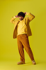 Wall Mural - Handsome Indian man in vibrant outfit posing on yellow backdrop.