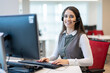 © Bojan - Happy young woman wearing headset communicating via conference call while speaking and looking at her camera in office.