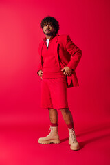 Wall Mural - Handsome young Indian man posing in a red jacket and shorts against a vivid red backdrop.