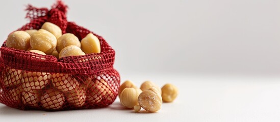 Aufkleber - Macadamia nuts are presented in a red mesh bag set against a white backdrop with copy space image.