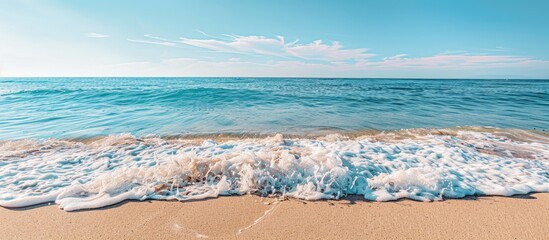 Wall Mural - Ocean waves gently lapping the sandy shore create a calming scene with a breathtaking view of the horizon and a clear blue sky in the background with copy space image.