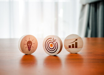 Poster - Target icon, creative light bulb symbol and growth graph sign on round wooden blocks on wood table and white background. Business strategy, action plan, goal and success process management concept.