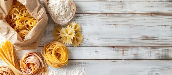 Poster - Top view of various uncooked pasta types and flour in a paper bag on a white wooden table with copy space image.