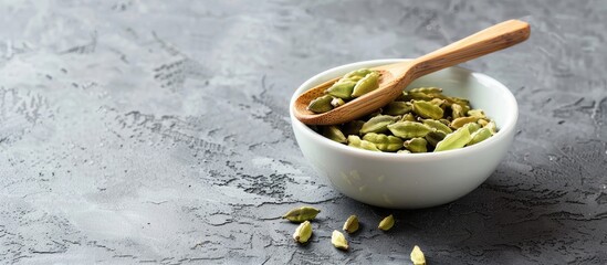 Sticker - A white ceramic bowl and bamboo spoon hold green cardamom (Elettaria cardamomum) on a gray concrete backdrop, emphasizing healthy eating with copy space image.