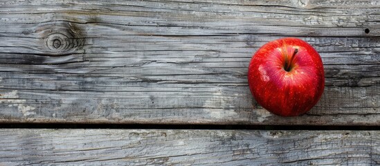 Sticker - A vibrant red apple resting on a rustic brown frame atop a gray wooden surface in a top-down view with copy space image included.