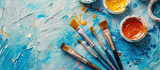 Poster - Close up of watercolor paints and brushes on a blue background with copy space image available