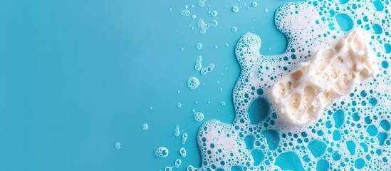 Poster - Cleaning sponge with soapy foam on a blue background conveying a cleaning concept Banner layout with a top view perspective and copy space image