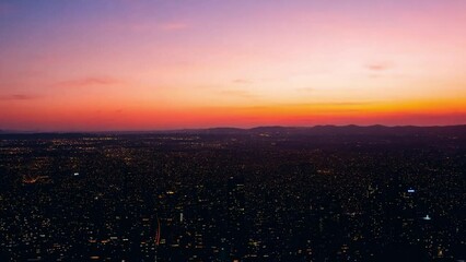 Aufkleber - A panoramic view of a city at sunset, with the sun setting behind a line of hills.