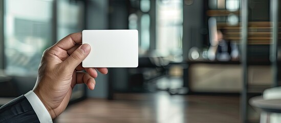 Poster - A businessman s hand holding a business card against an office background with copy space image