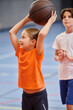 © LIGHTFIELD STUDIOS - A young girl joyfully holds a basketball high up in the air, radiating a sense of excitement and passion for the game.