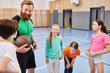 © LIGHTFIELD STUDIOS - A man teacher holds a basketball while a diverse group of children stand around him in a bright, lively classroom setting.