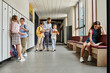© LIGHTFIELD STUDIOS - A group of individuals, including a man teacher, standing in a hallway by lockers, engaged in conversation and instruction.