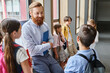 © LIGHTFIELD STUDIOS - A bearded man stands confidently in front of a group of children in a vibrant classroom, engaging them in an educational activity.