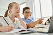 © LIGHTFIELD STUDIOS - children sitting at a table in a bright classroom, focused on a laptop screen