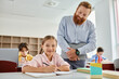 © LIGHTFIELD STUDIOS - A man teacher in a classroom standing beside a little girl, both engaged in learning and teaching.