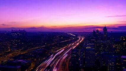 Aufkleber - A city skyline is bathed in the warm glow of sunrise, with a highway winding through the cityscape.