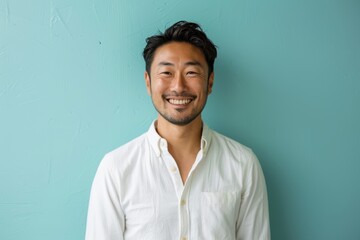 Wall Mural - Portrait of a blissful asian man in his 40s wearing a simple cotton shirt while standing against solid pastel color wall