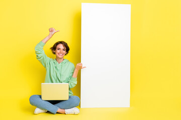 Sticker - Full length photo of cheerful sweet girl dressed green sweatshirt pointing thumbs modern device empty space isolated yellow color background