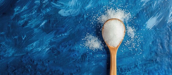 Wall Mural - Ceramic spoon with sugar crystals displayed on a blue backdrop with copy space image