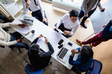 Wall Mural - Top view of multiracial creative business men in white and black formal clothes disputing at a meeting using gadgets during the conference while sitting at the modern office.