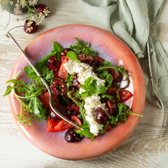 Wall Mural - ceramic plate with salad with stracciatella cheese, cherries and tomatoes on the table