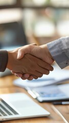 Aufkleber - Close-up of a business handshake over a desk with documents and a laptop. Concept of partnership, agreement, and professional collaboration. Ideal for business and corporate themes
