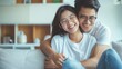 © PAPAGAP - Happy young couple in casual clothes, smiling and embracing each other while sitting on a cozy couch in a bright, modern living room.