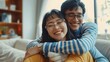 © PAPAGAP - Happy couple with glasses hugging and smiling at home, showcasing love, affection, and happiness in a cozy living room setting.