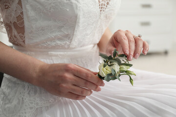 Wall Mural - Bride holding boutonniere for her groom on blurred background, closeup