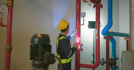 Wall Mural - Professional engineer worker man in safety uniform holding flashlight checking maintenance the industry pipeline pump system construction under the building factory