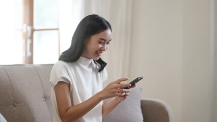 Wall Mural - Asian girl looking at mobile phone and smiling, Enjoying on smart phone