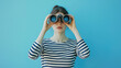 © Creative Art7 - Young woman in a striped shirt looking through binoculars isolated on a blue background with copy space for text