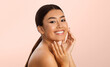 © Prostock-studio - A young Asian woman with long brown hair tied back in a ponytail smiles brightly while touching her face with both hands. She is standing against a light pink background.