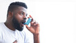 © Prostock-studio - An image of African American man using an inhaler to treat his asthma. He is holding the inhaler in his right hand and has his mouth open. He is wearing a white t-shirt, copy space