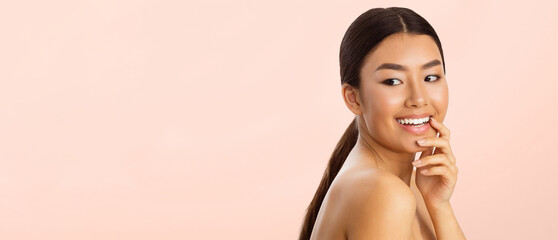 Wall Mural - Asian young woman smiling and looking to the side. She has long, dark hair pulled back in a ponytail and is wearing no clothing above the shoulders, panorama with copy space