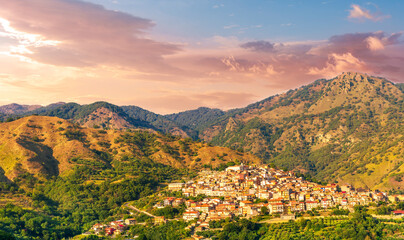 Wall Mural - highland landscape of italian town between amazing green mountains with scenic sunset cloudy sky on background