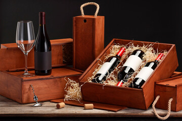 Wall Mural - Boxes with wine bottles and glass on wooden table against black background