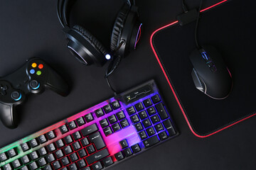 Wall Mural - Computer mouse, RGB keyboard, game controller and headset on black background, flat lay