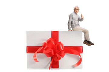 Wall Mural - Elderly man sitting on a present and gesturing thumbs up