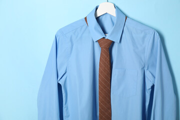 Wall Mural - Hanger with shirt and brown necktie on light blue background