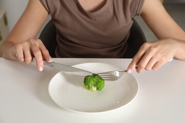 Wall Mural - Eating disorder. Woman holding cutlery near broccoli at white table indoors, closeup