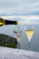 Wall Mural - Pouring of cold sparkling wine, cava or champagne in two glasses on table with sea water view