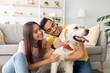 © Prostock-studio - Portrait of happy multiracial couple scratching their pet dog, sitting on floor at home. Arab guy and his Caucasian girlfriend hugging their golden retriever in living room